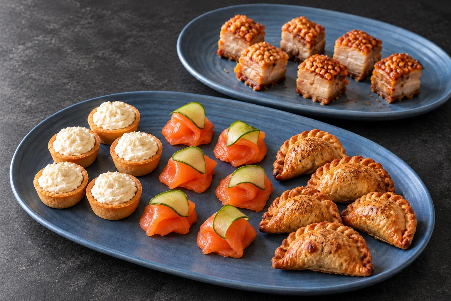 Cocktail canapés with tartlets, salmon cucumber bites, empanadas and pork belly on charcoal stone